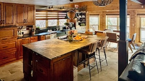 A rustic kitchen with wooden cabinets, a marble island, and a dining area with chairs.