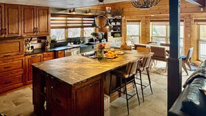 A rustic kitchen with wooden cabinets, a marble island, and a dining area with chairs.