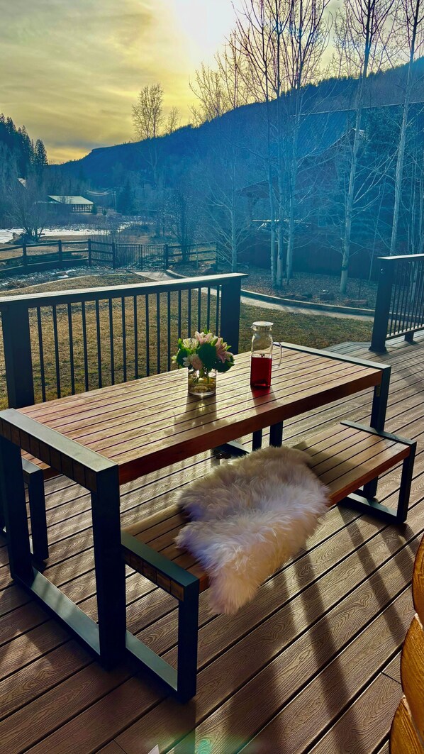 A wooden deck with a bench, a glass pitcher, and a vase of flowers.