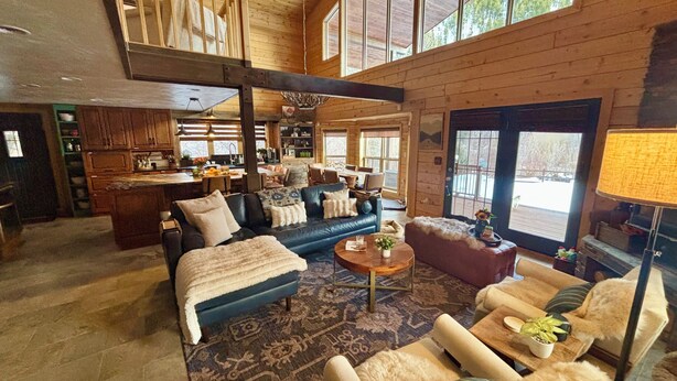 A spacious living area with a large sofa, a coffee table, and a fireplace. There is a kitchen area with wooden cabinets and a dining table.