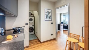 Een moderne keuken met een fornuis, een wasmachine en een eethoek met houten stoelen.