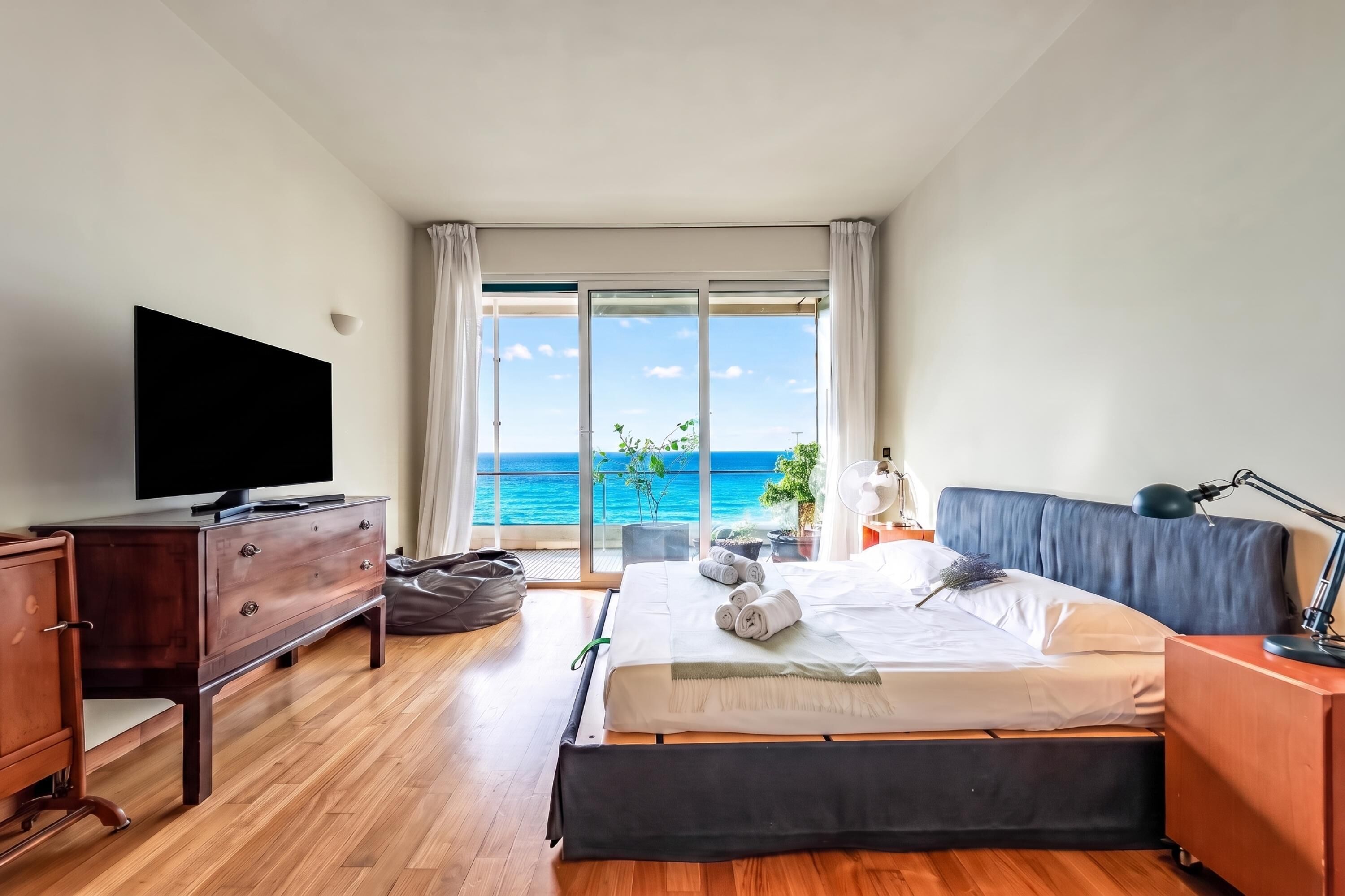 A hotel room with a large bed, a television, a desk, and a view of the ocean.