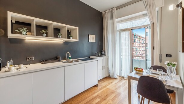 A modern kitchen with white cabinets, a built-in shelf with plants, a sink, and a dining area with a table and chairs. - Piazza Rossetti Apartments (Genoa)