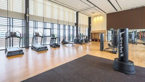 Ein geräumiger Fitnessraum mit unterschiedlichen Trainingsgeräten, großen Fenstern und Holzboden.