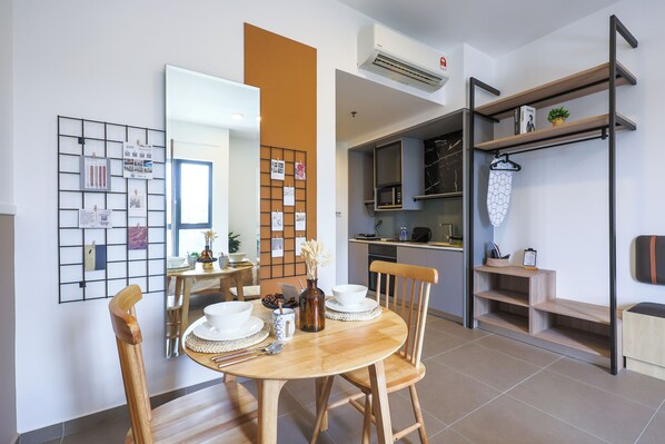 A modern dining area with a wooden table and chairs, a kitchen area with a microwave and shelves, and a wall-mounted rack with a plant. - Mossaz Suites by Mana Mana (Petaling Jaya)