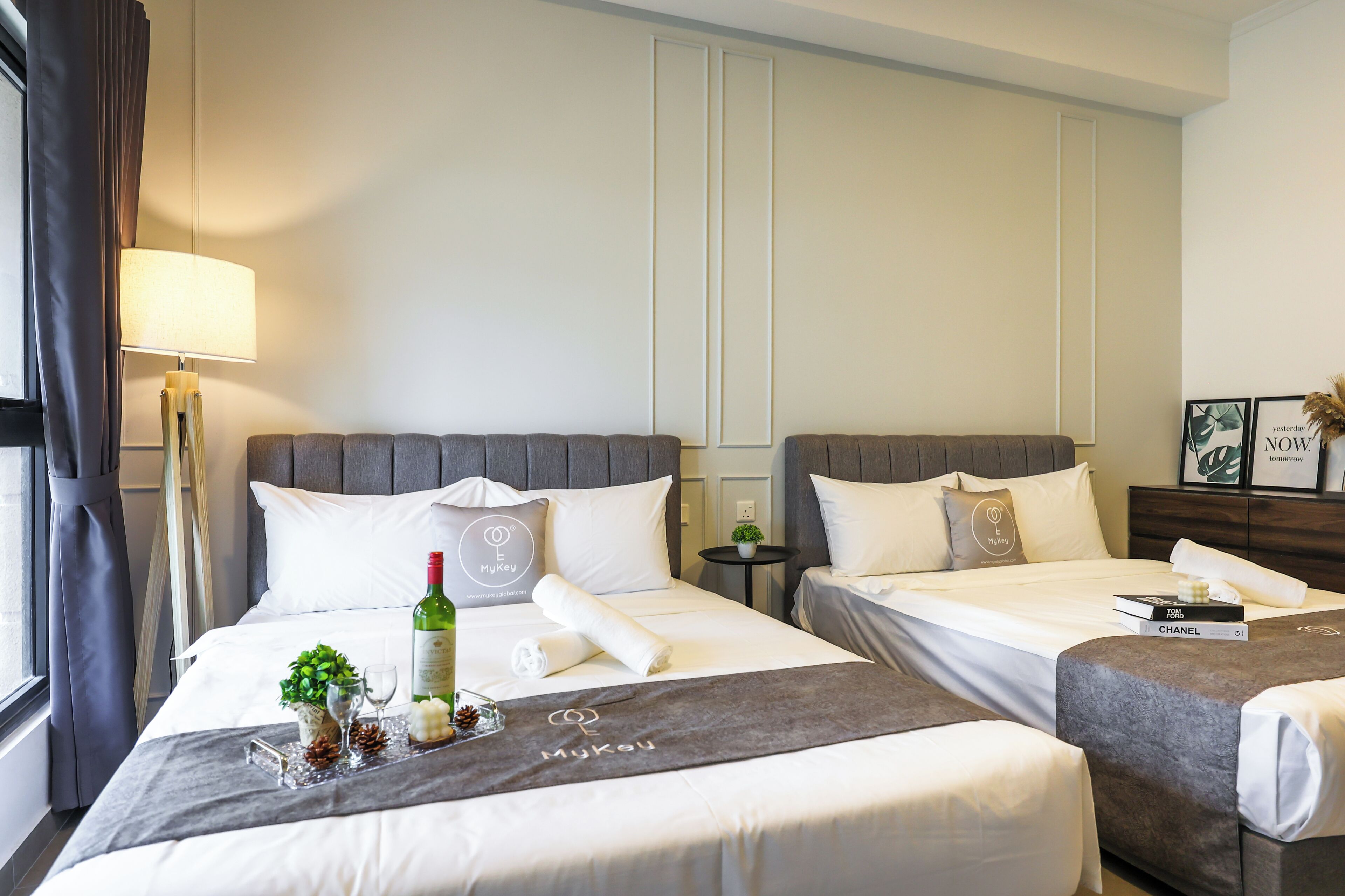 Una habitación de hotel con dos camas, una mesita de noche, una lámpara y una ventana con cortinas.