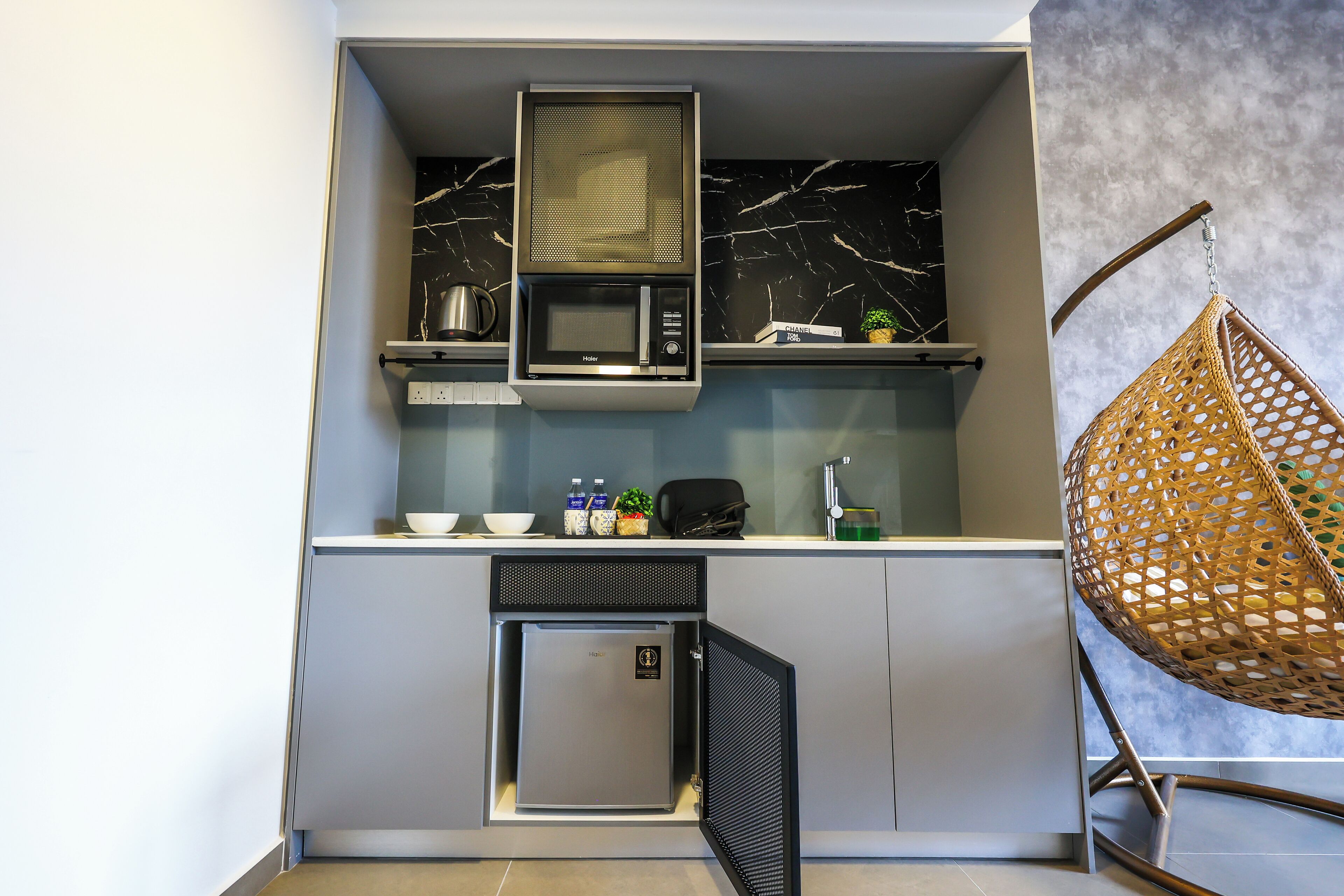 Een compacte keuken met een ingebouwde magnetron, een kleine koelkast en een hangstoel.