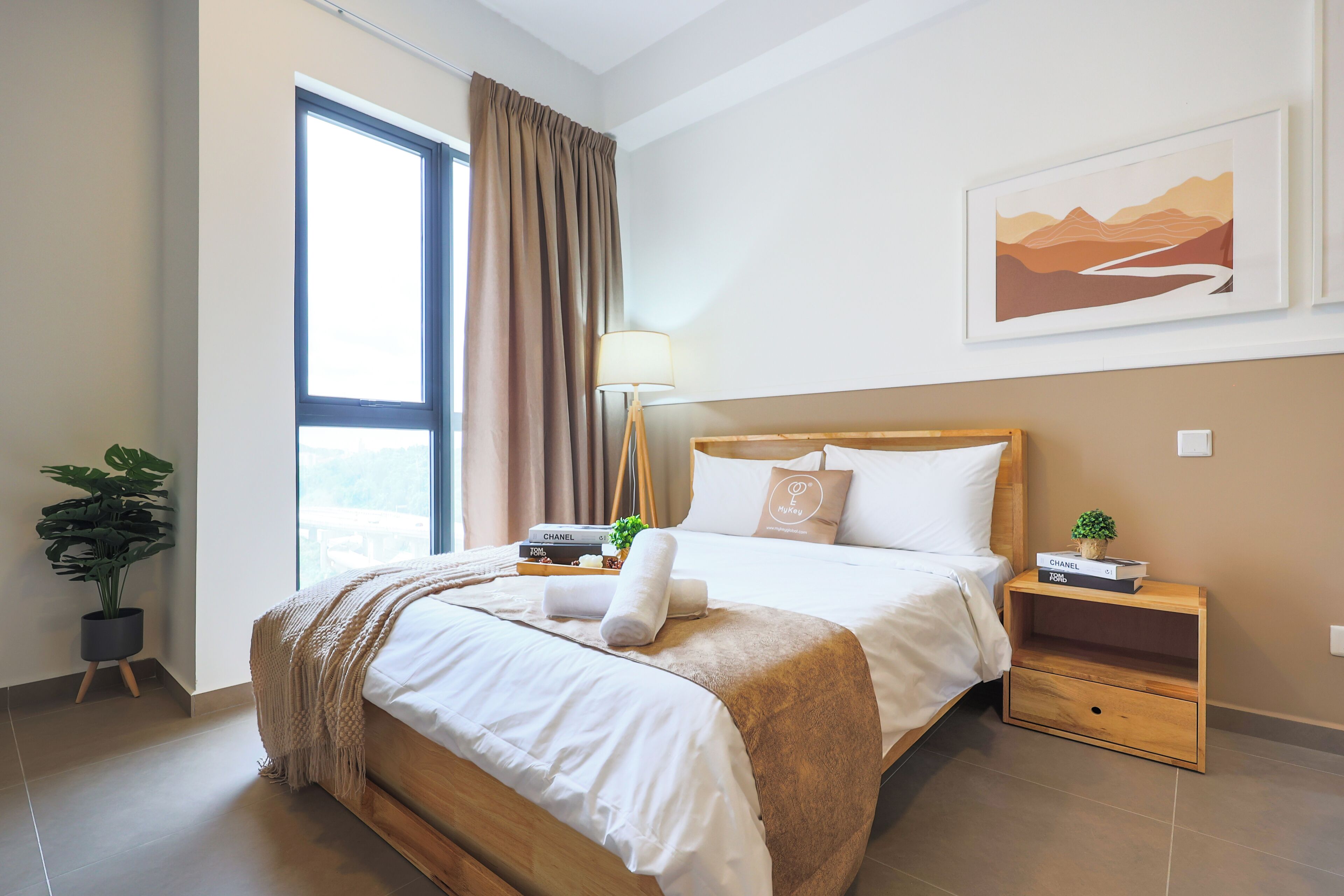 A neatly made bed with a wooden headboard, a bedside table with a lamp, a framed picture on the wall, and a potted plant.