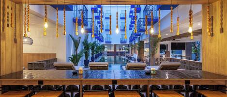A spacious indoor area with a long table and multiple chairs, a staircase with blue railings, and hanging wooden light fixtures.