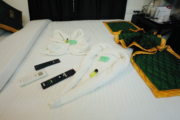 A neatly made bed with towels, remote controls, and a green quilted blanket. - NIRA Residency (Thiruvananthapuram)