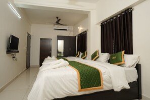A hotel room with a bed, a television, an air conditioning unit, and a ceiling fan. - NIRA Residency (Thiruvananthapuram)