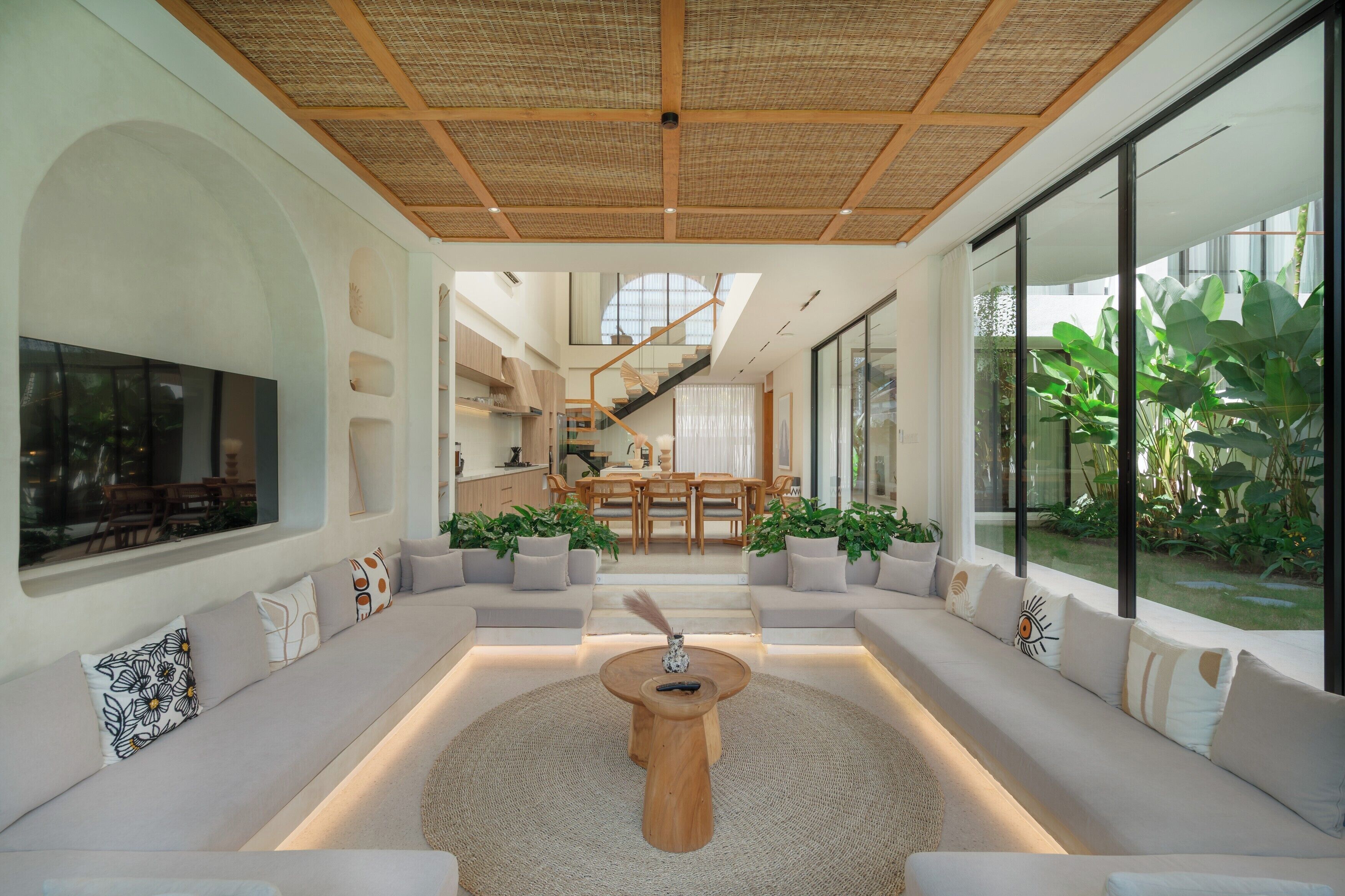 Un interior moderno con una zona de estar central, una escalera y ventanas grandes.
