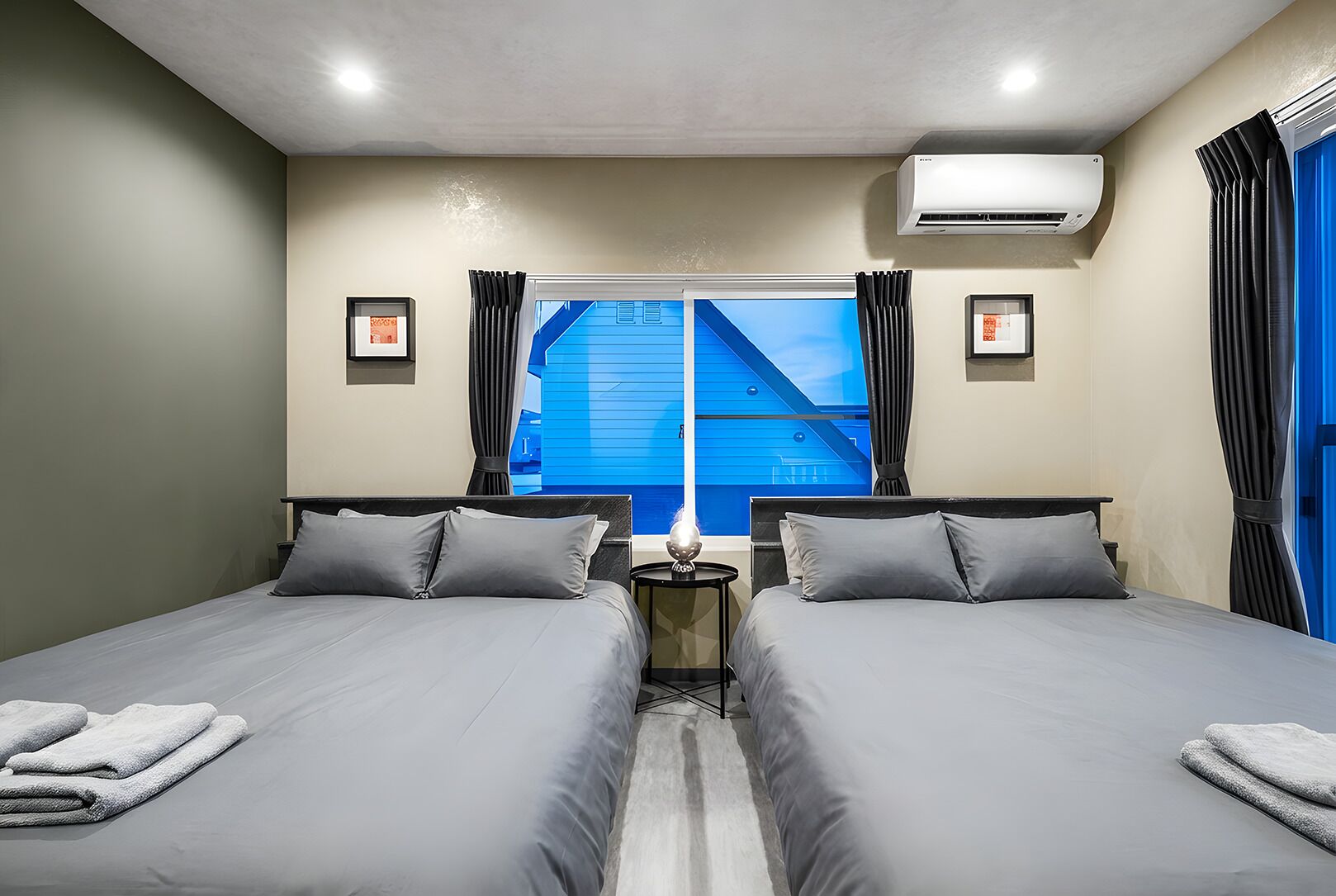 Habitación de hotel con dos camas, una mesita de noche, un aire acondicionado y una ventana con cortinas.