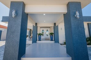 Ein moderner Gebäudeeingang mit flachem Dach, zwei große Kübelpflanzen und blauem Himmel.