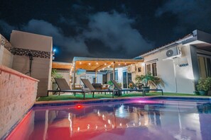 Ein Swimmingpool mit Liegestühlen, eine überdachte Terrasse und ein Gebäude mit Klimaanlage.