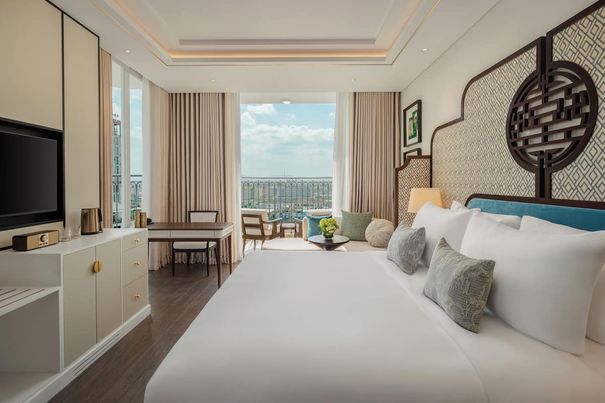 Ein Hotelzimmer mit einem großen Bett, einem Fernseher, einem Schreibtisch und einem Balkon mit Blick.