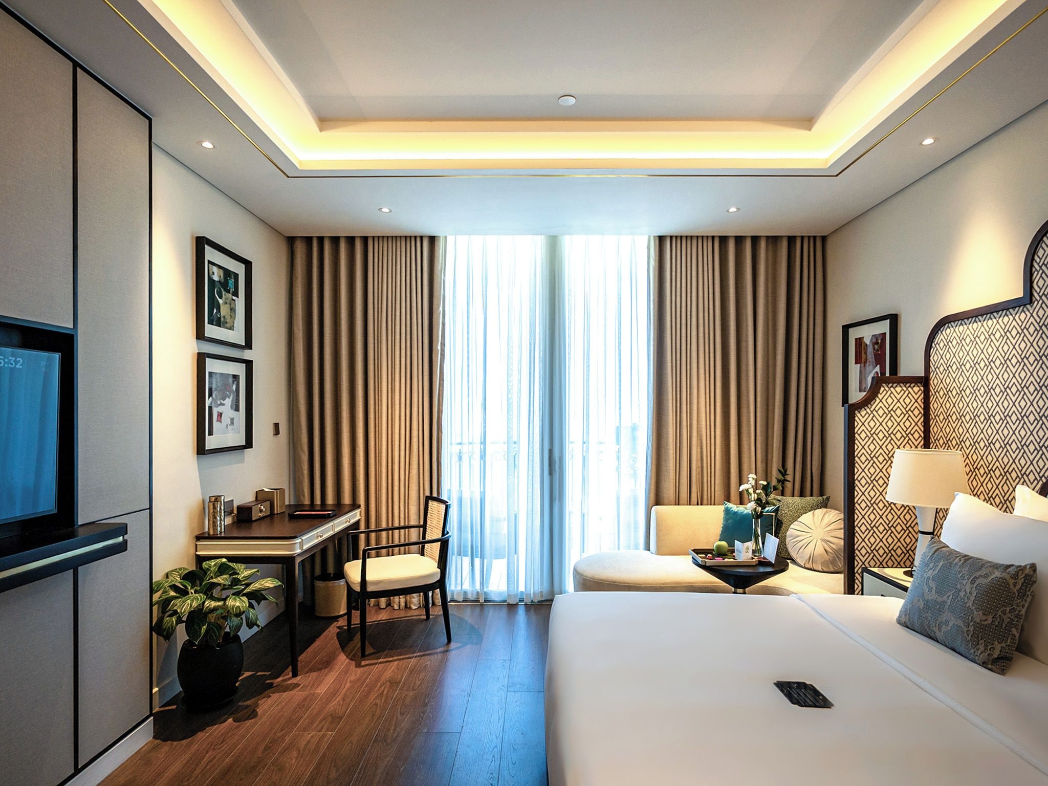 A hotel room with a bed, a desk, a chair, a TV, a sofa, and a window with curtains.