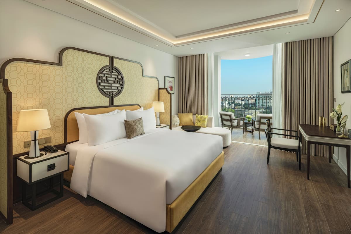 Ein Hotelzimmer mit einem großen Bett, einem Schreibtisch und einem Balkon mit Blick auf die Stadt.
