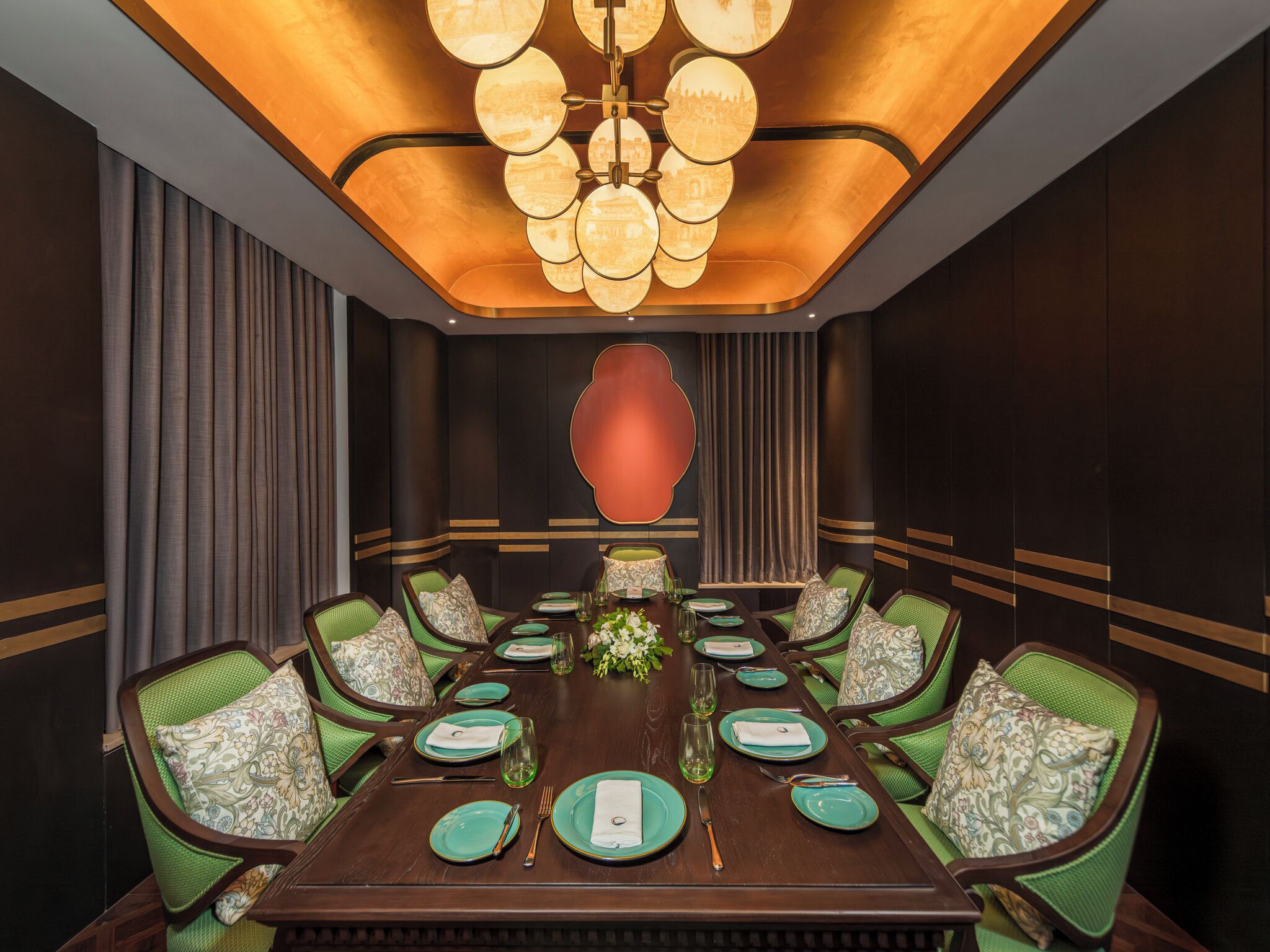 A conference room with a long table, green chairs, and a central chandelier.