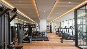 A modern gym with various exercise equipment, large windows, and a wooden floor. - Grand Royal Riverside Hue, Fusion Collection (Hue)
