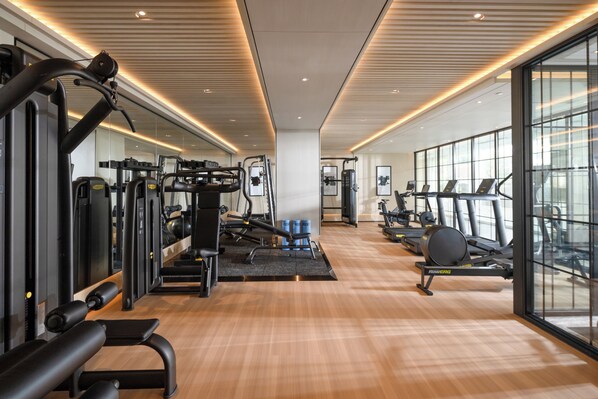 Une salle de sport moderne équipée de divers appareils d’exercice, dotée de grandes fenêtres et d’un plancher en bois.