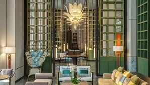 A spacious living area with a sofa, chairs, and a coffee table. There is a chandelier hanging from the ceiling and a large window with green frames. - Grand Royal Riverside Hue, Fusion Collection (Hue)