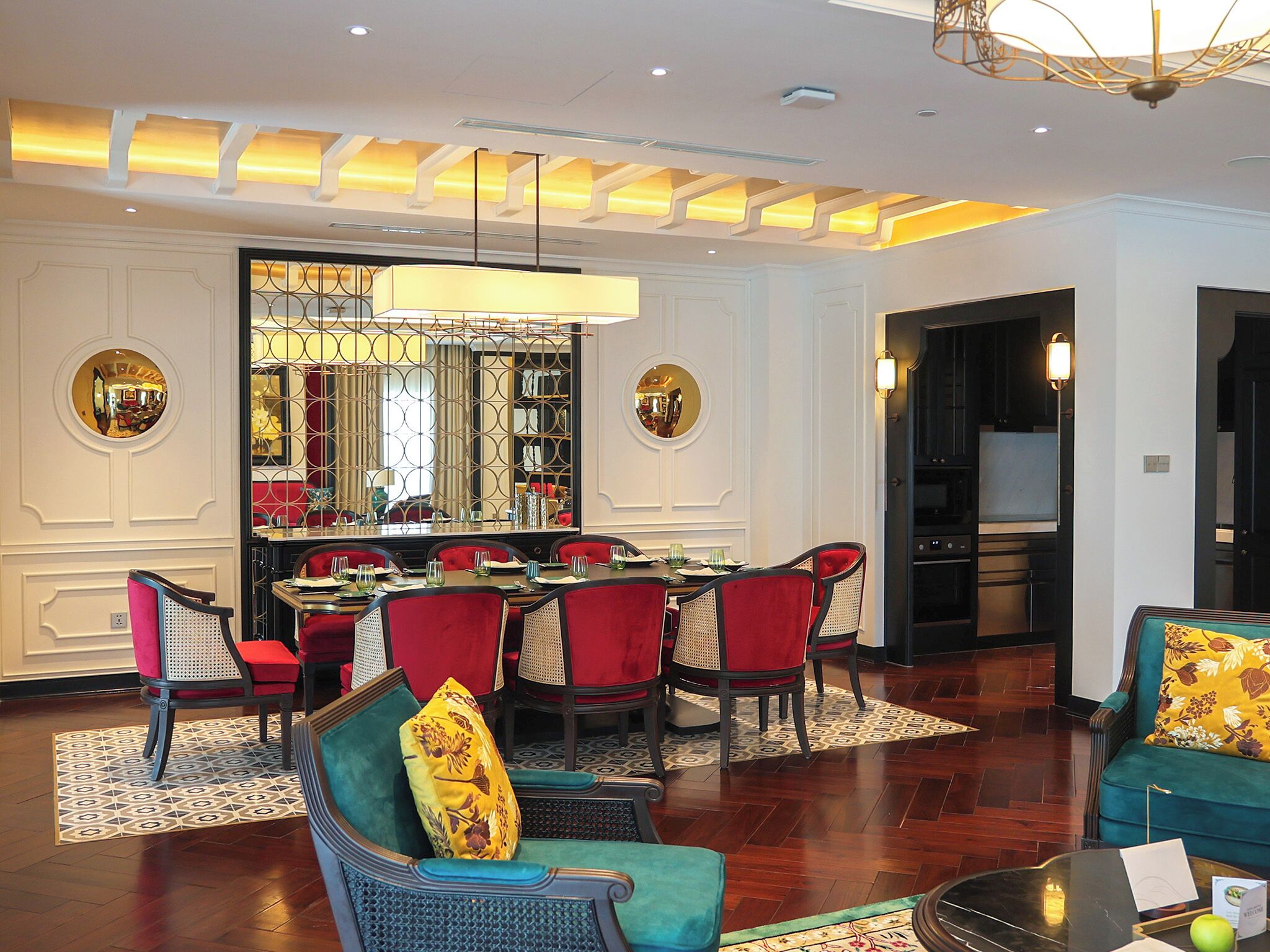Un'area pranzo con un tavolo rotondo e sedie rosse, un soggiorno con divani color acquamarina e tappeti decorati, e un moderno design del soffitto con illuminazione a incasso.