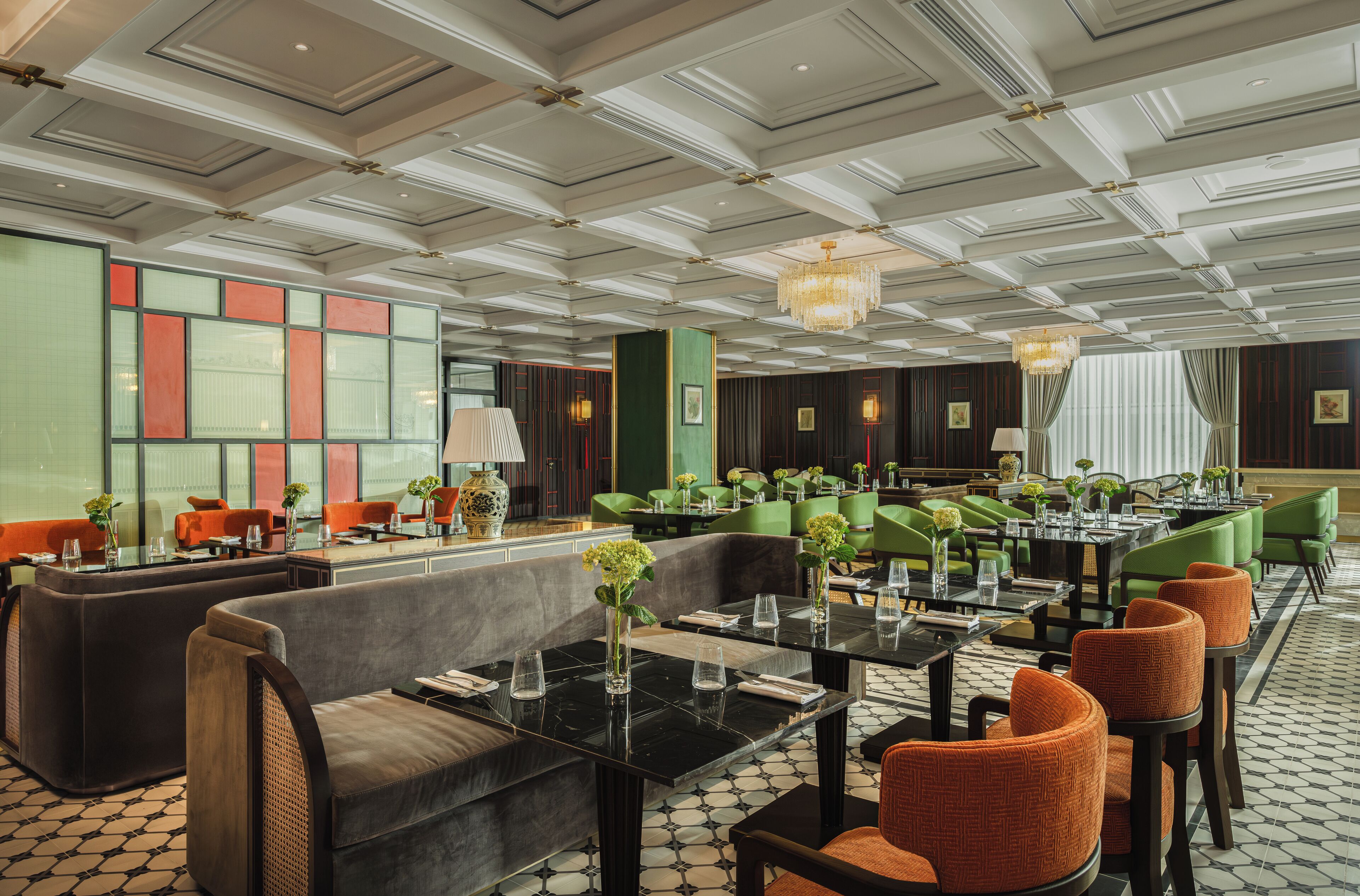 A spacious hotel lobby with a high ceiling, green seating areas, and a patterned floor.