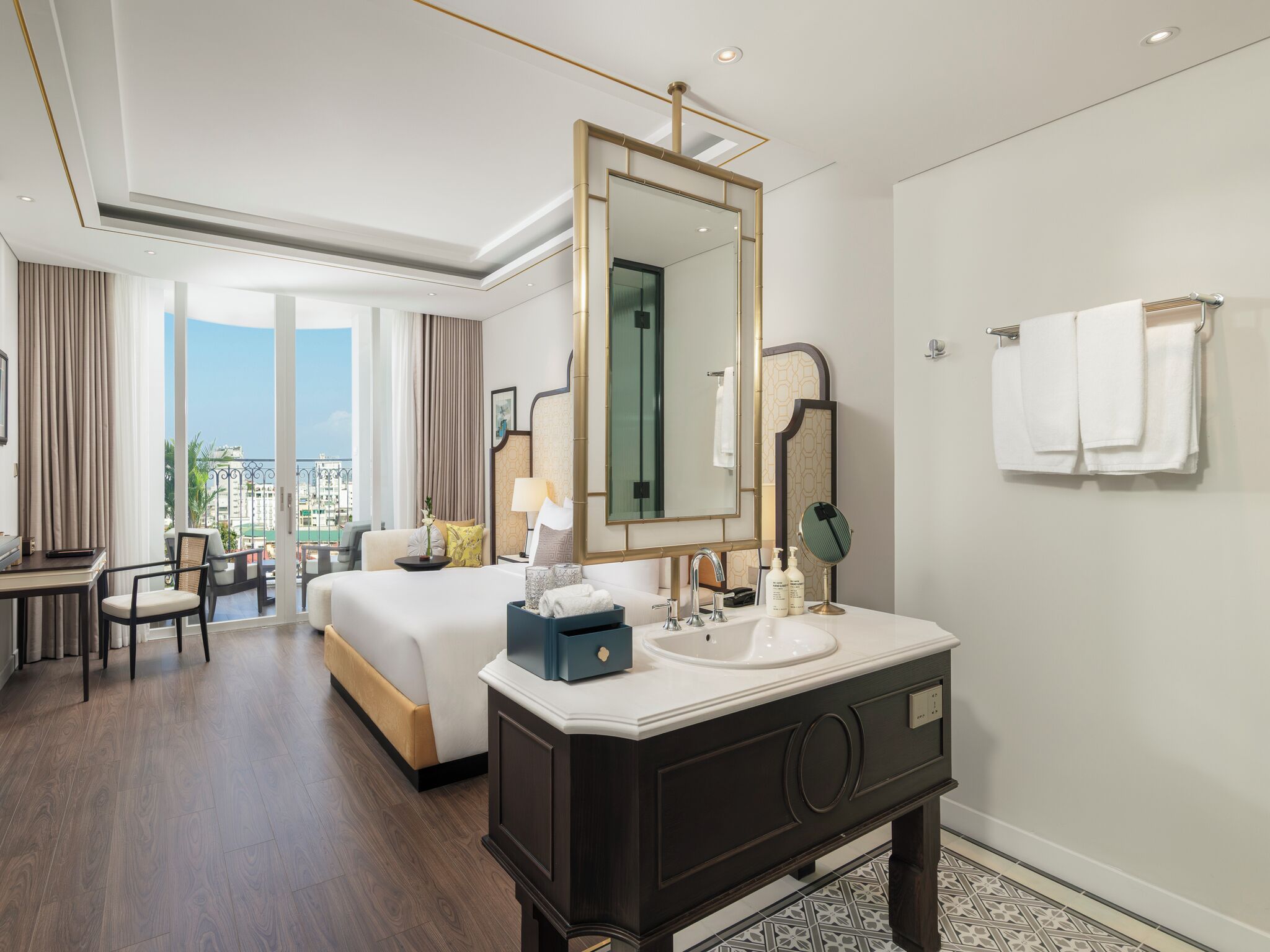 A hotel room with a large bed, a desk, a bathroom with a mirror, and a view of the city.