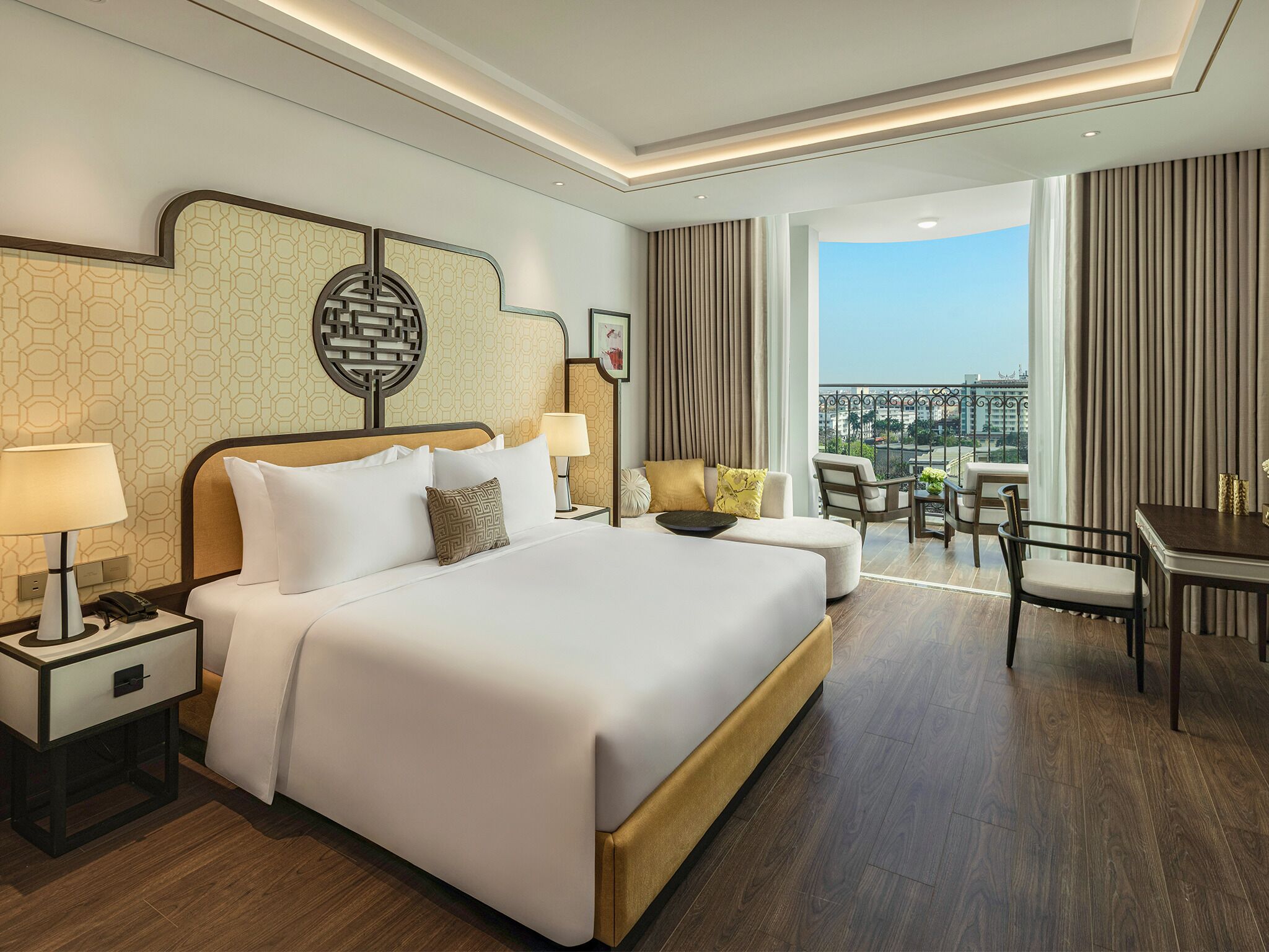 A hotel room with a large bed, bedside tables, a desk, and a view of the city.