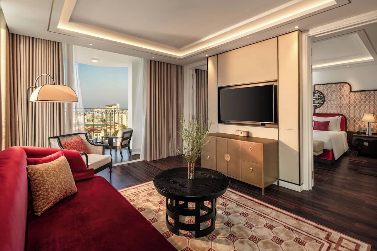 Ein modernes Hotelzimmer mit einem roten Sofa, einem runden schwarzen Tisch, einem Fernseher und Blick auf die Stadt.