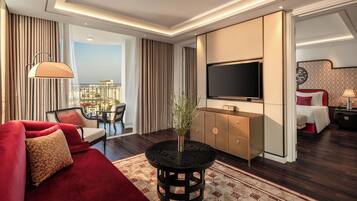 Une chambre d’hôtel moderne avec un canapé rouge, une table ronde noire, un téléviseur et une vue sur la ville.