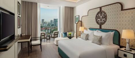 A hotel room with a bed, bedside tables, a TV, a desk, and a view of the city.