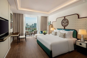 Habitación de hotel con cama, mesitas de noche, televisor, escritorio y vistas a la ciudad.