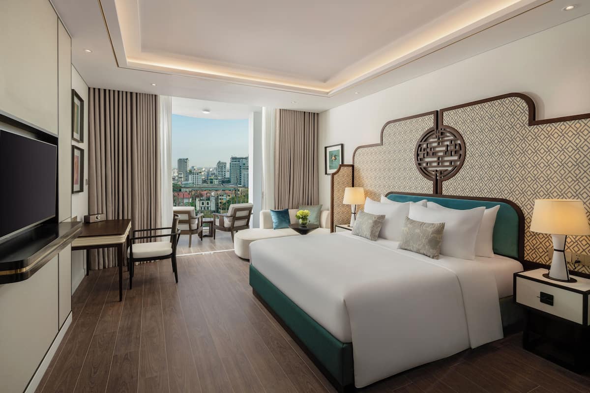 Ein Hotelzimmer mit einem großen Bett, einem Fernseher, einem Schreibtisch mit Stuhl und Blick auf die Stadt.