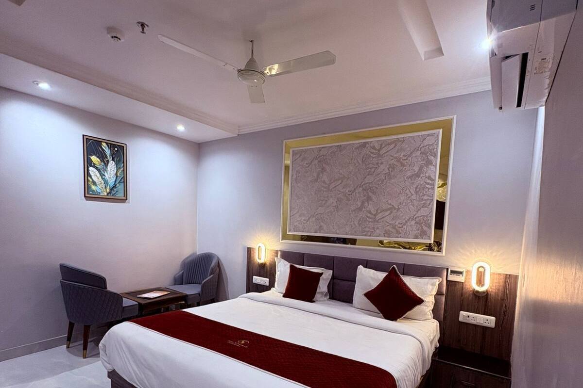 A modern hotel room with a large bed, a desk, a chair, a ceiling fan, and a wall-mounted artwork.
