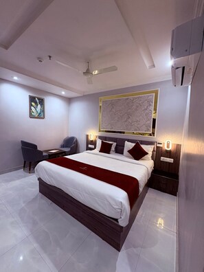 A modern hotel room with a large bed, a desk, a chair, a ceiling fan, and a wall-mounted artwork. - Hotel Sundaram Continental  (Prayagraj)