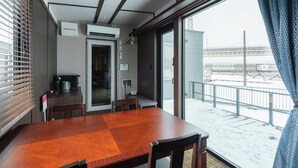 Un coin repas avec une table et des chaises en bois, un espace cuisine équipé d’appareils électroménagers, et une vue sur un paysage enneigé par de grandes fenêtres.