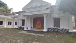 Un edificio con una entrada central flanqueada por columnas, una puerta de madera grande y un patio con baldosas.