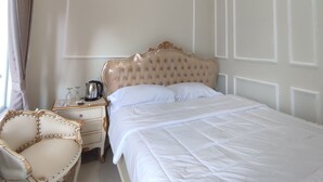 Un dormitorio ordenado con una cama grande, una mesita de noche, una silla y una ventana con cortinas.