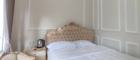 A neatly arranged bedroom with a large bed, a bedside table, a chair, and a window with curtains.