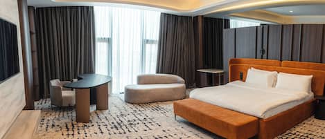 A modern hotel room with a large bed, a small table, a chair, and a sofa.