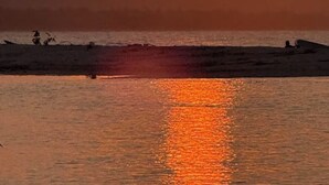Solnedgang over vand med bjerge i baggrunden.