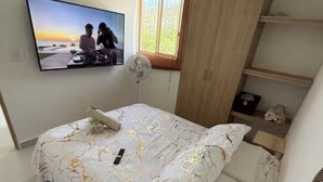 Et soveværelse med seng, fjernsyn på væggen, et vindue og en ventilator.