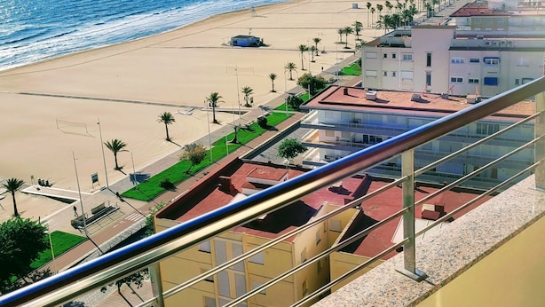 Vista sulla costa dal balcone, con spiaggia sottostante, edifici e palme sullo sfondo.