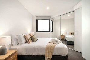 Une chambre d’hôtel moderne, avec un lit soigneusement fait, une table de chevet avec une lampe et un grand miroir qui reflète la pièce.