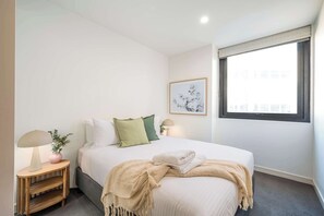 A neatly arranged bedroom with a bed, bedside lamps, a small table with a lamp, a vase with flowers, and a framed picture on the wall. - Cinema by the Sea - Movie Nights & Coastal Vibes (Newcastle)