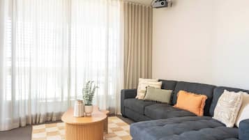 A living room with a dark grey sofa, a round wooden coffee table, and a checkered rug.