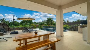 Un espacio exterior amplio con mesa y bancos de madera, piscina y parrilla.