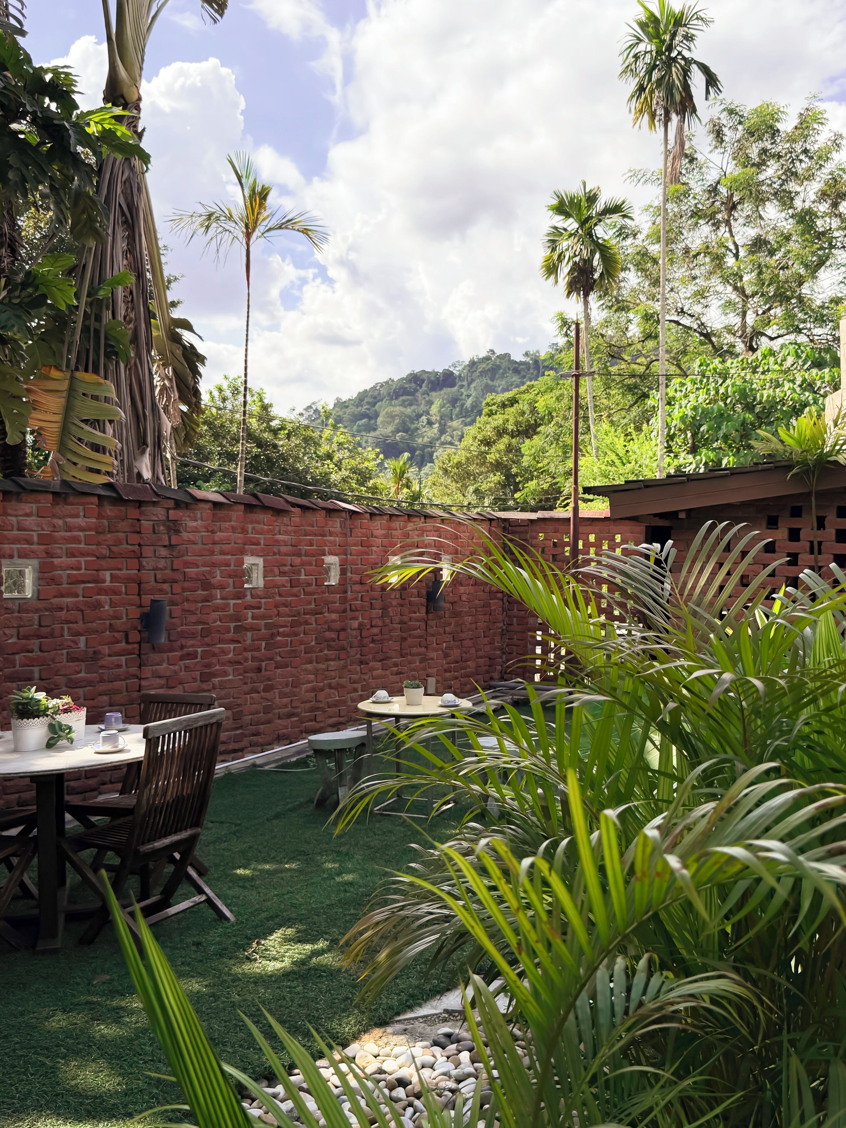 A patio area with a brick wall, a round table with chairs, and a small garden with rocks and plants.